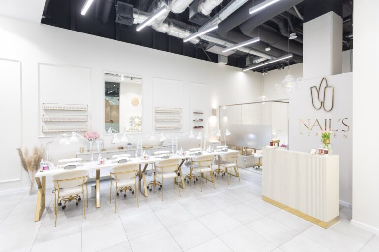 Salon paznokci Nails Heaven w Katowicach - pięć stanowisk do manicure z białymi fotelami i złotymi detalami, ściana z lakierami hybrydowymi i recepcja z logo salonu.